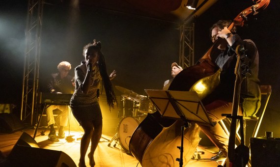 Chanteuse et ses musiciens sur scène dans une semi-pénombre avec halo doré.