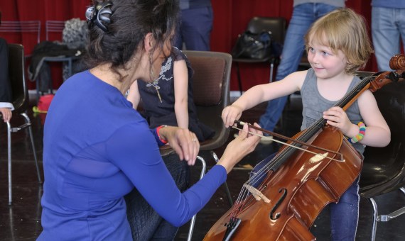 Un adulte accompagne un enfant dans la découverte du violoncelle.