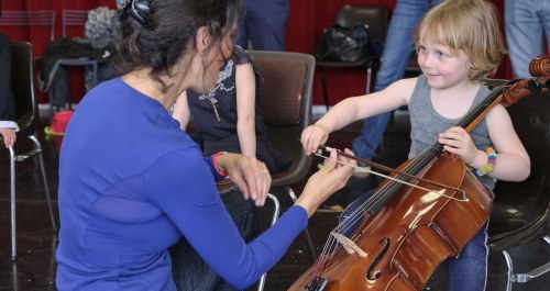 Un adulte accompagne un enfant dans la découverte du violoncelle.