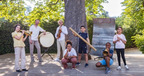 Musiciens, enfants et instruments posant à l'ombre d'un arbre.