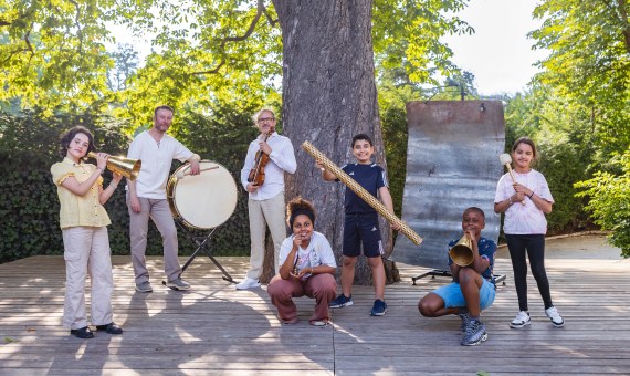 Musiciens, enfants et instruments posant à l'ombre d'un arbre.